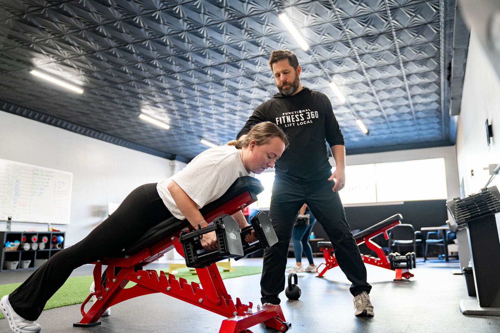 Coach guiding a member through a supported dumbbell row